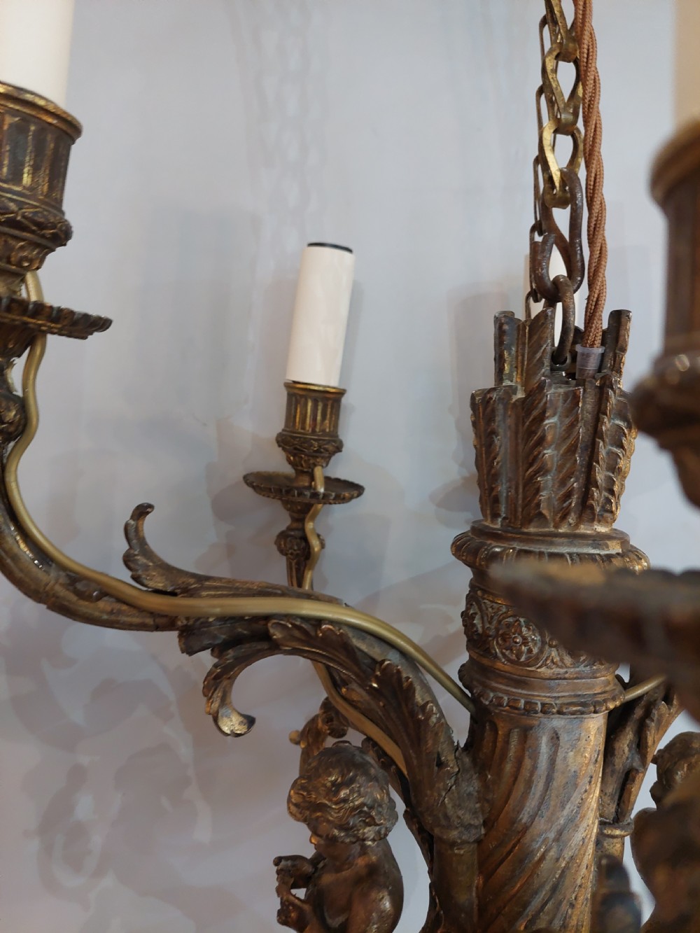 An early 20th-century six-arm gilt metal chandelier featuring carved cherub figures, scrolling acanthus leaf branches, and white candle sleeves. View V