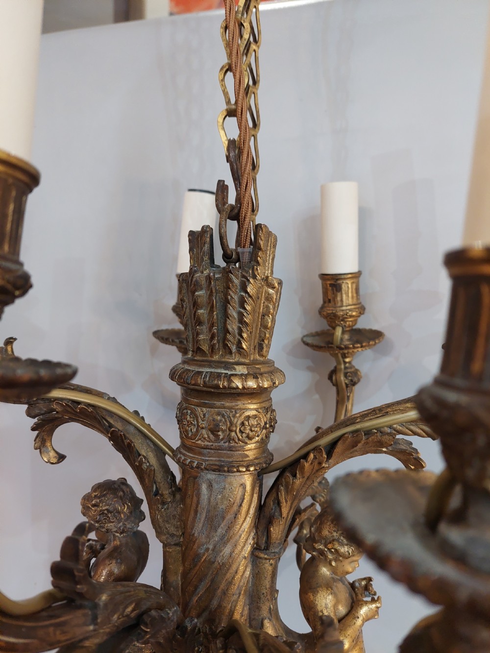 An early 20th-century six-arm gilt metal chandelier featuring carved cherub figures, scrolling acanthus leaf branches, and white candle sleeves. View VI