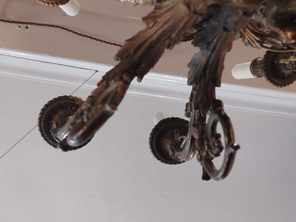 An early 20th-century six-arm gilt metal chandelier featuring carved cherub figures, scrolling acanthus leaf branches, and white candle sleeves. View VII