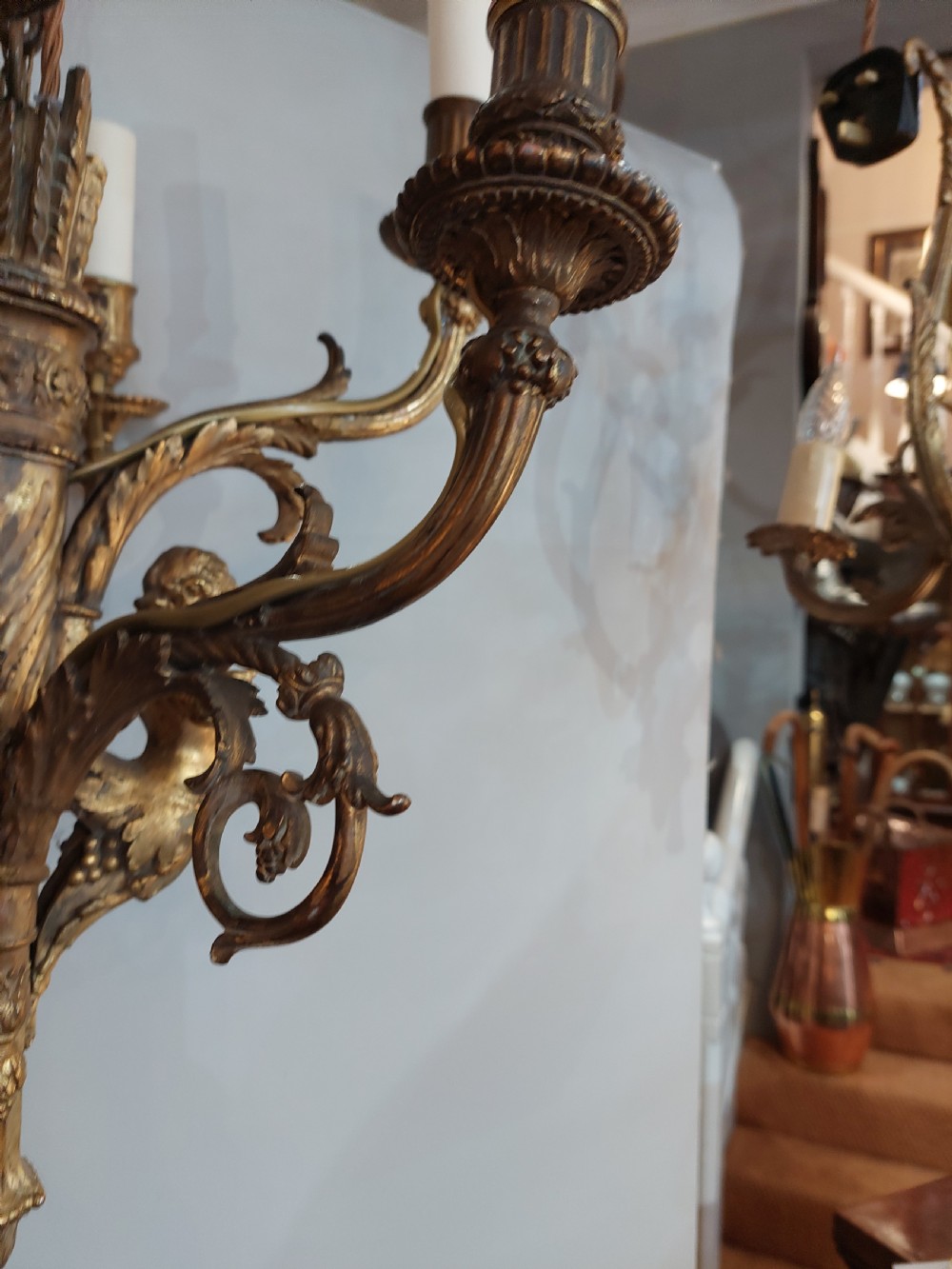 An early 20th-century six-arm gilt metal chandelier featuring carved cherub figures, scrolling acanthus leaf branches, and white candle sleeves. View VIII