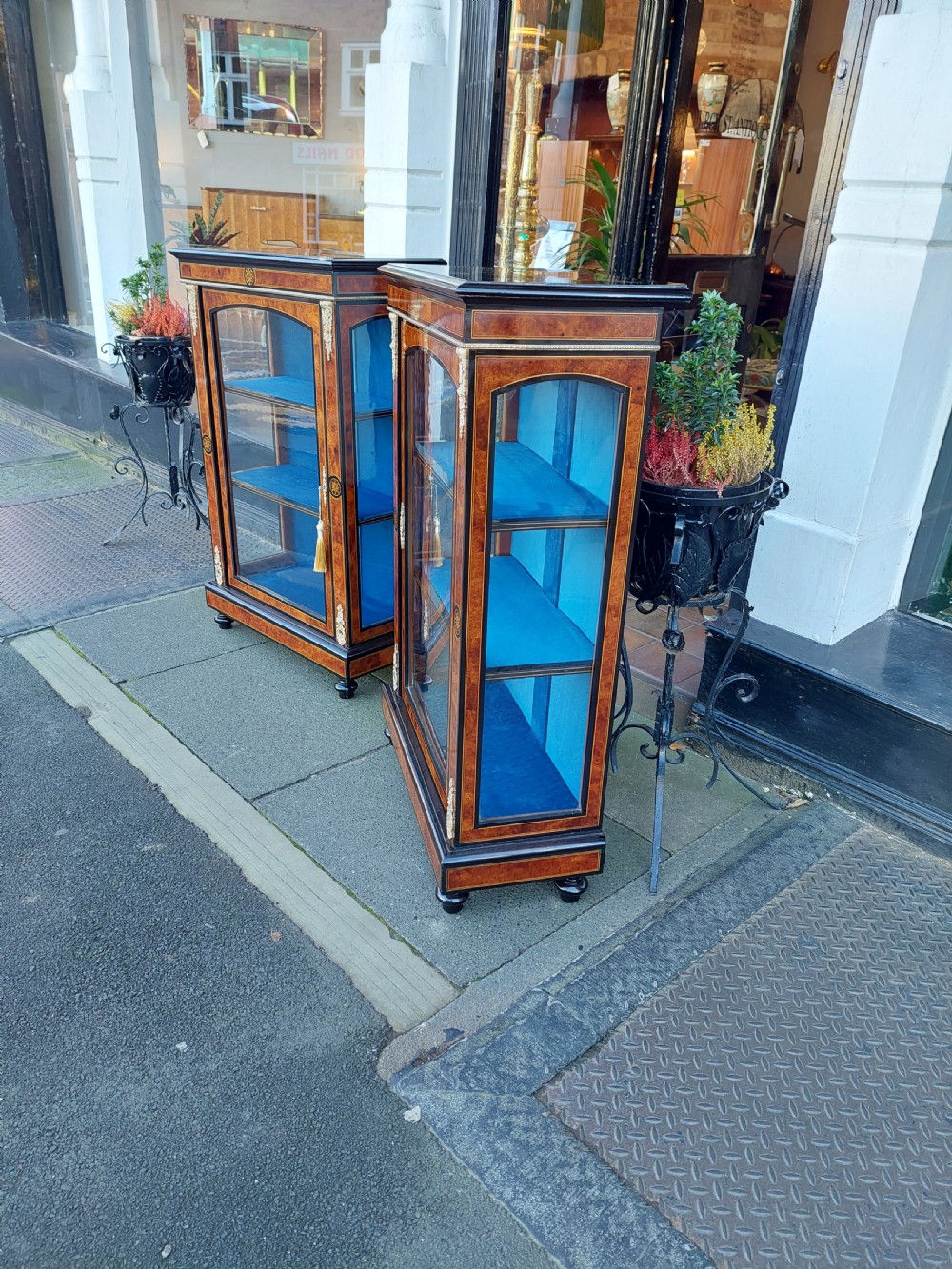 A pair of Victorian burr walnut display cabinets featuring ebonised borders, marquetry inlay, brass mounts, single glazed doors, and blue velvet lined shelves. View III