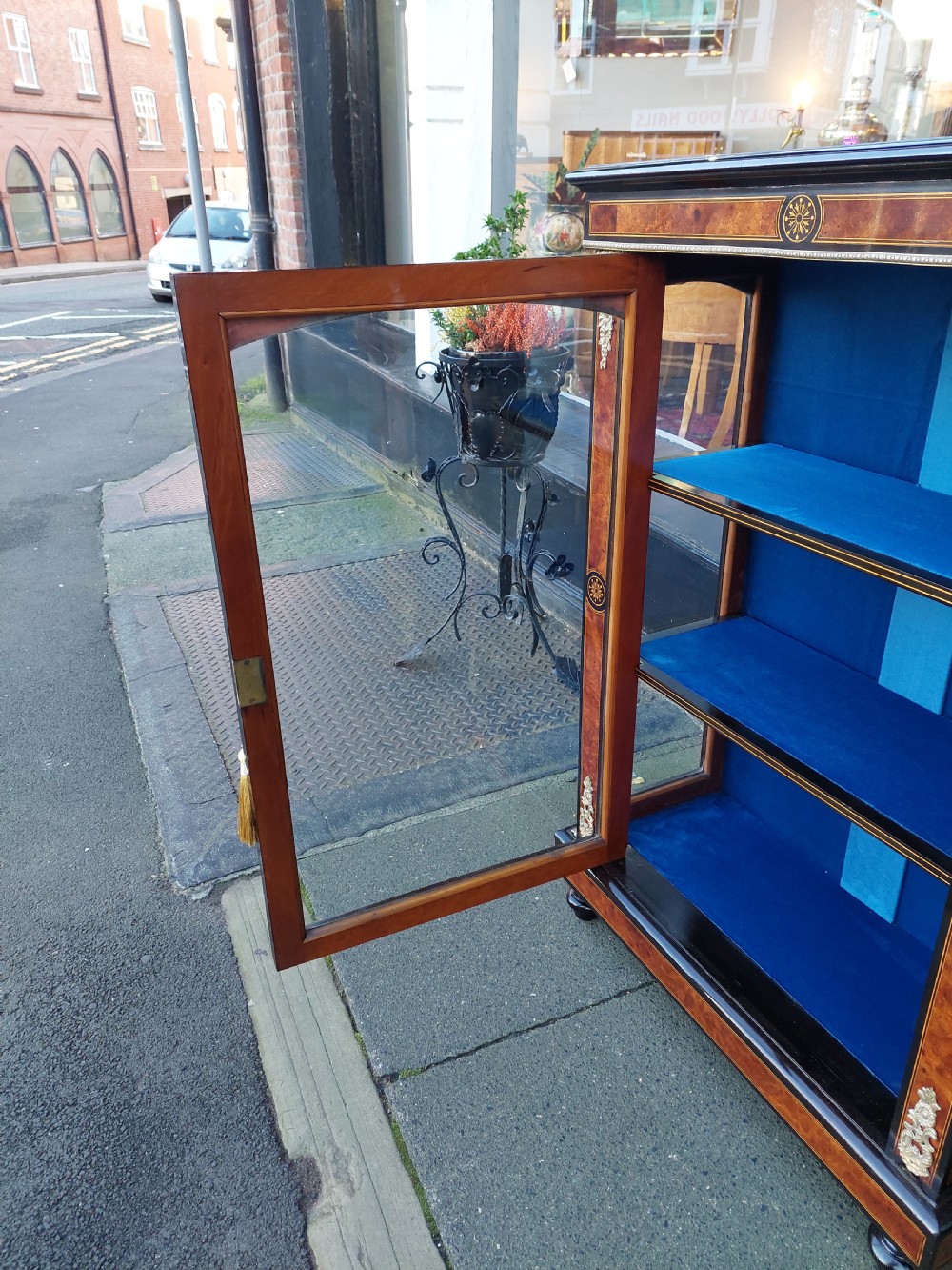 A pair of Victorian burr walnut display cabinets featuring ebonised borders, marquetry inlay, brass mounts, single glazed doors, and blue velvet lined shelves. View IX