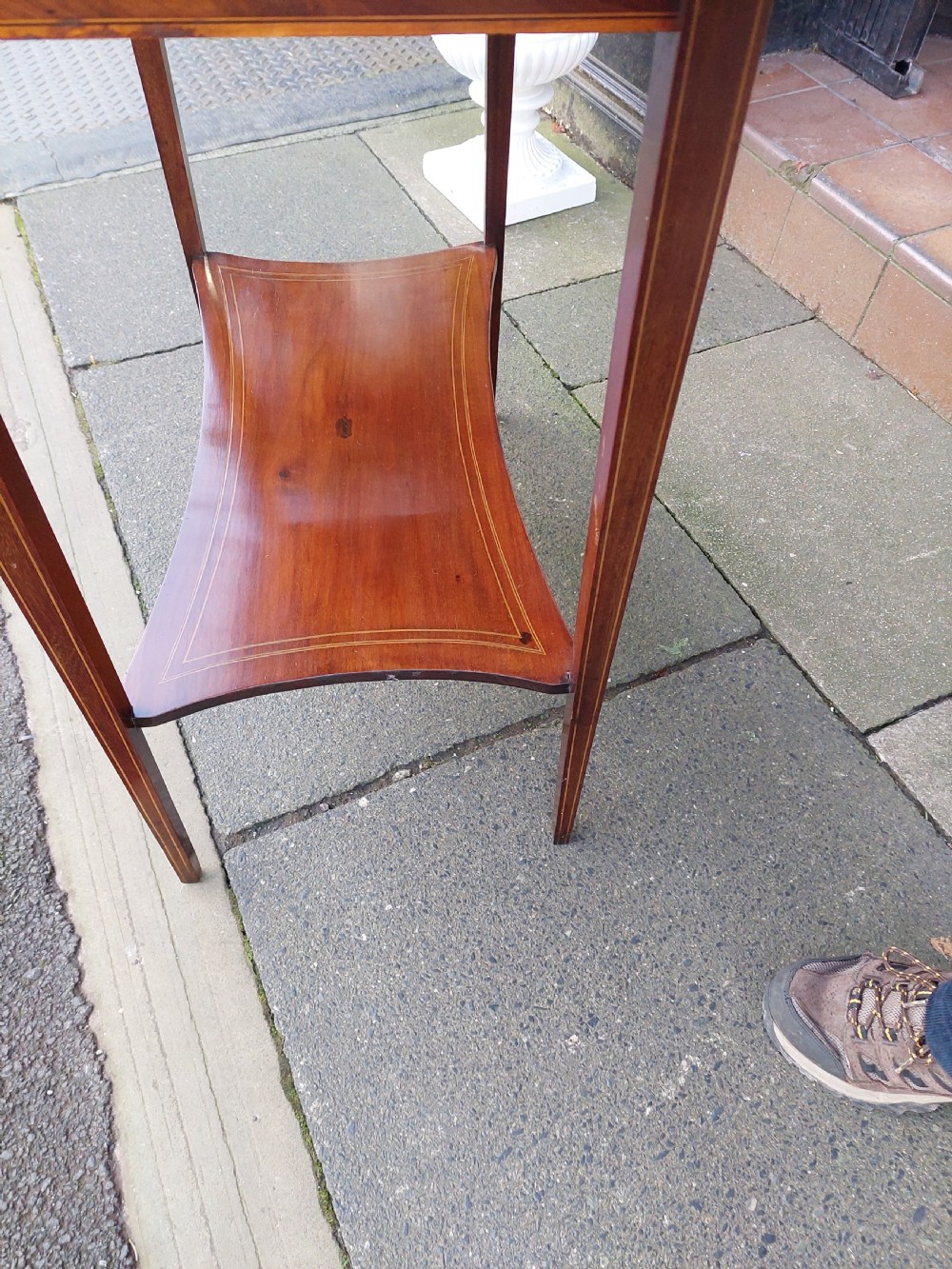 An Edwardian mahogany side table with a central oval marquetry inlay on top, fine stringing on slender tapered legs, and a shaped lower shelf. View V