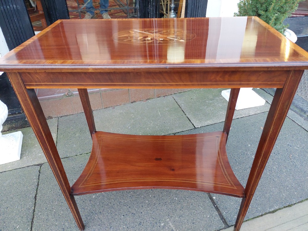 An Edwardian mahogany side table with a central oval marquetry inlay on top, fine stringing on slender tapered legs, and a shaped lower shelf. View VI