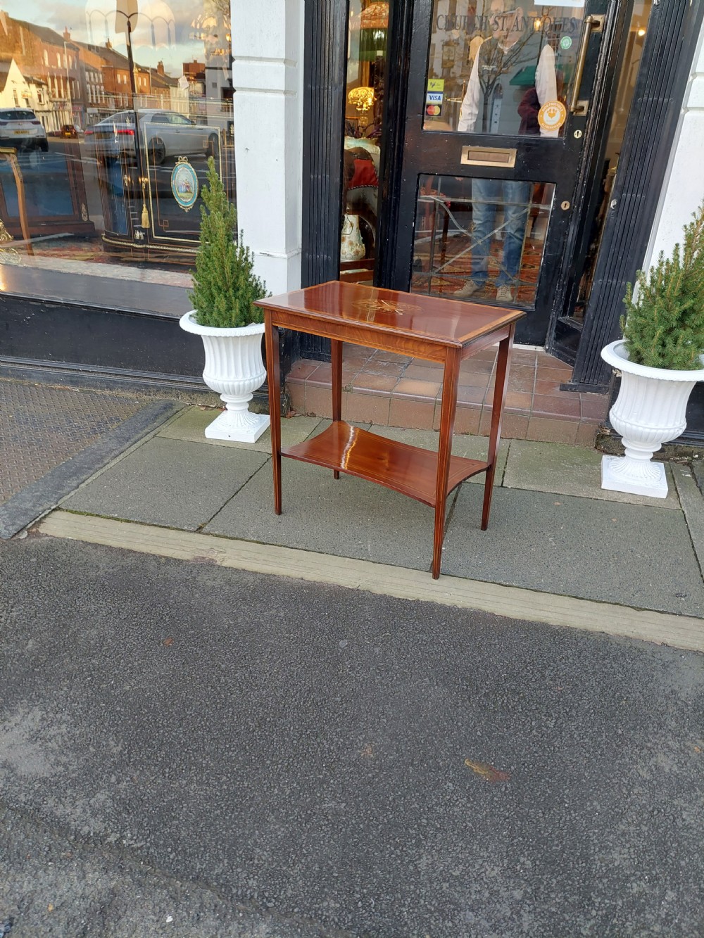 An Edwardian mahogany side table with a central oval marquetry inlay on top, fine stringing on slender tapered legs, and a shaped lower shelf. View VII