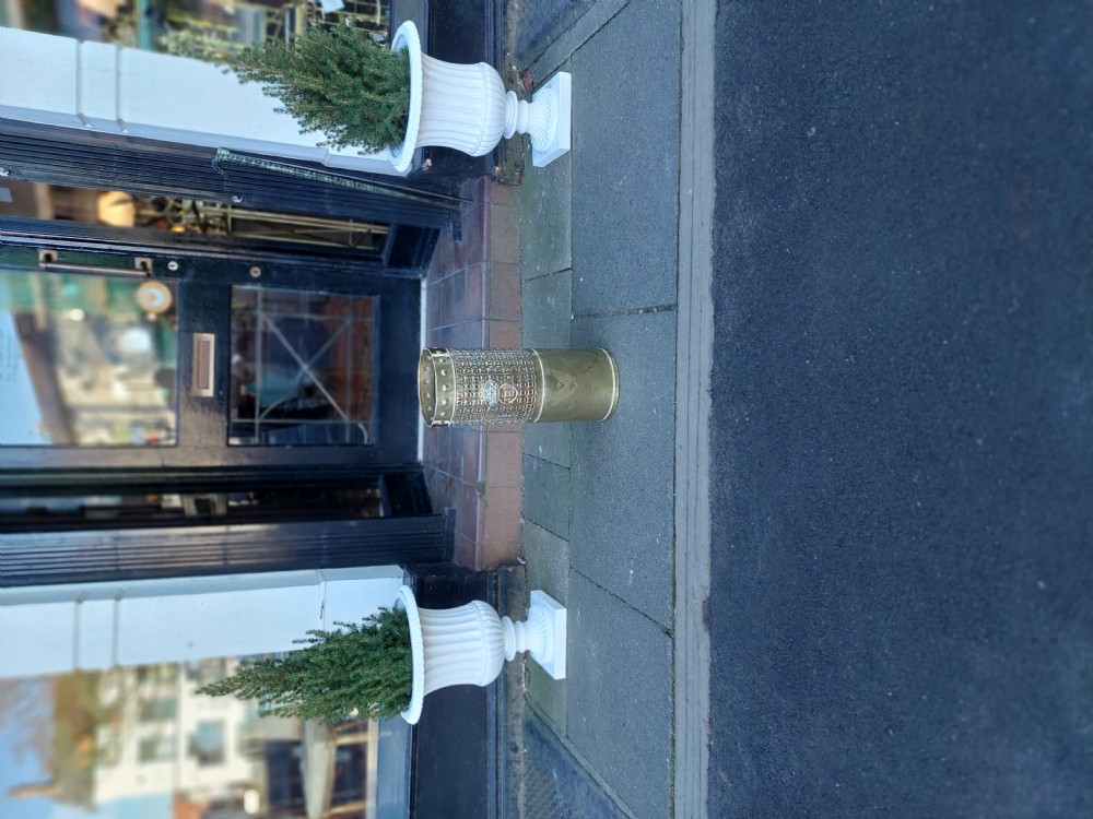 A cylindrical Victorian brass stick stand featuring a pierced lattice midsection, riveted top rim, and a central lion mask ring handle. View VIII