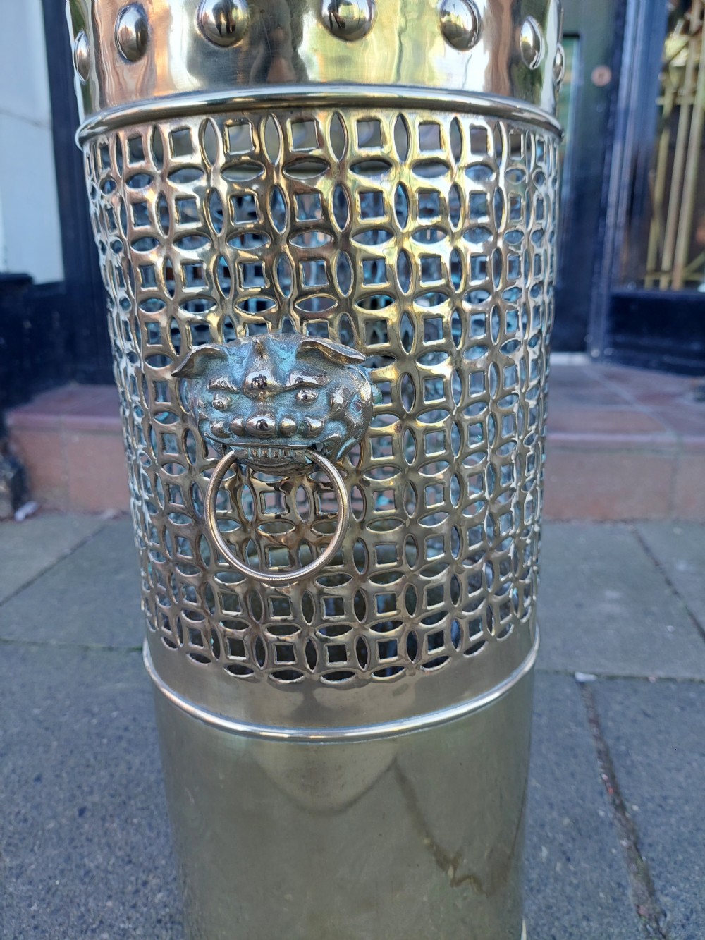 A cylindrical Victorian brass stick stand featuring a pierced lattice midsection, riveted top rim, and a central lion mask ring handle. View XIV