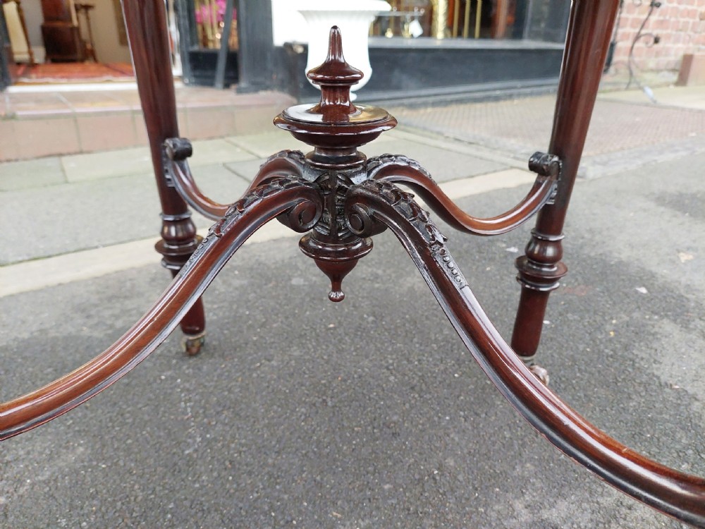A late 19th-century mahogany centre table featuring a shaped top with marquetry inlay, turned legs, crossed stretcher with central finial, and brass castors. View IV