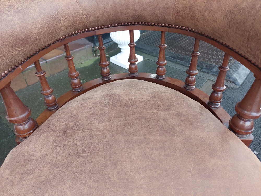A late 19th-century walnut captains chair featuring a curved brown leather padded backrest with brass stud detailing, turned spindles, and legs set on castors. View III