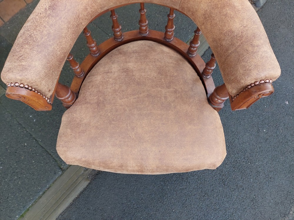 A late 19th-century walnut captains chair featuring a curved brown leather padded backrest with brass stud detailing, turned spindles, and legs set on castors. View IV