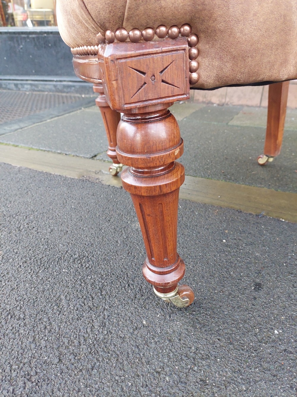 A late 19th-century walnut captains chair featuring a curved brown leather padded backrest with brass stud detailing, turned spindles, and legs set on castors. View V