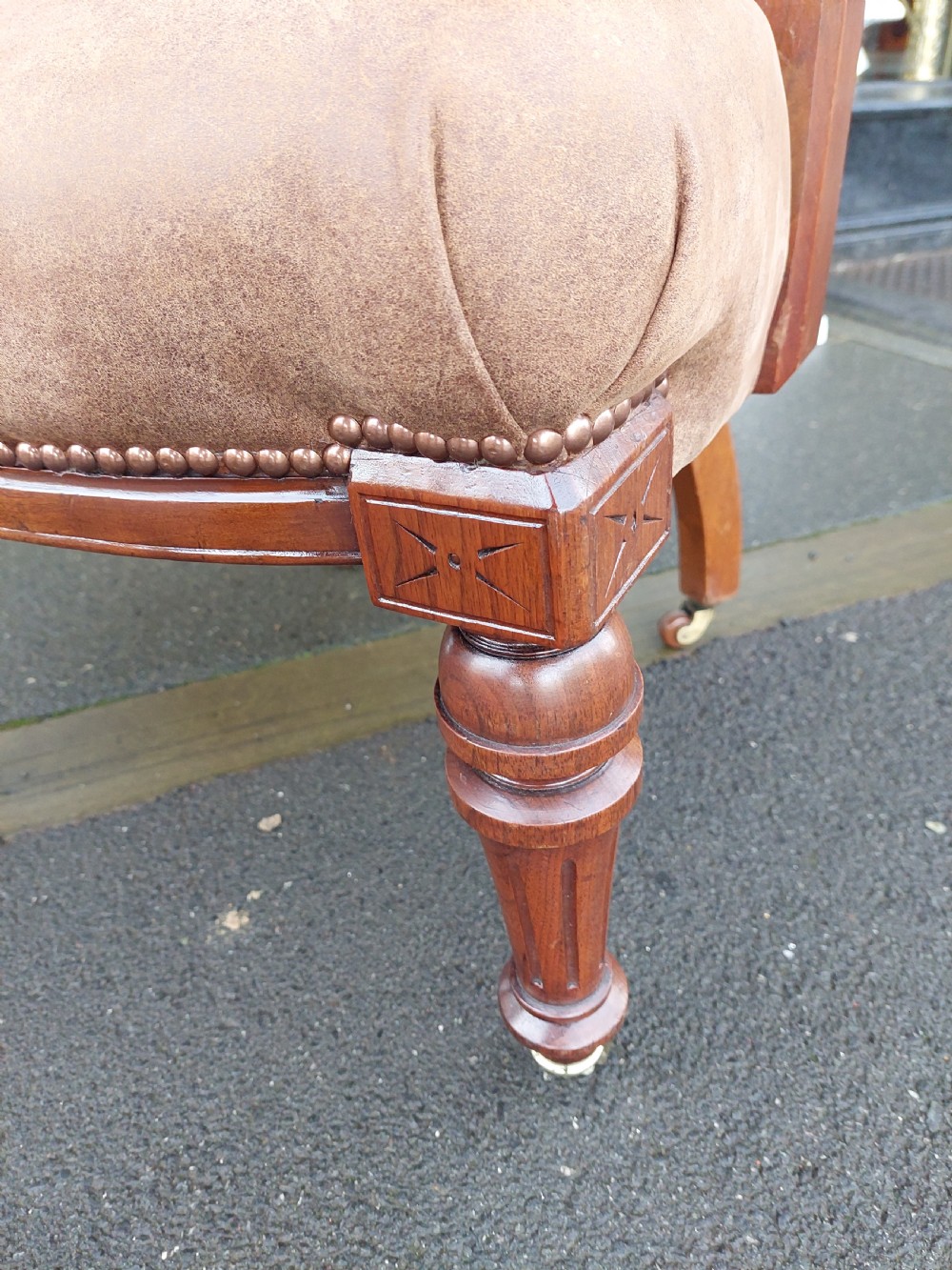 A late 19th-century walnut captains chair featuring a curved brown leather padded backrest with brass stud detailing, turned spindles, and legs set on castors. View VI