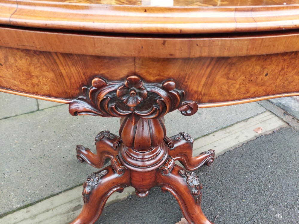 A Victorian burr walnut card table featuring a serpentine-shaped folding top resting on a carved pedestal support and quadripartite cabriole legs with castors. View II