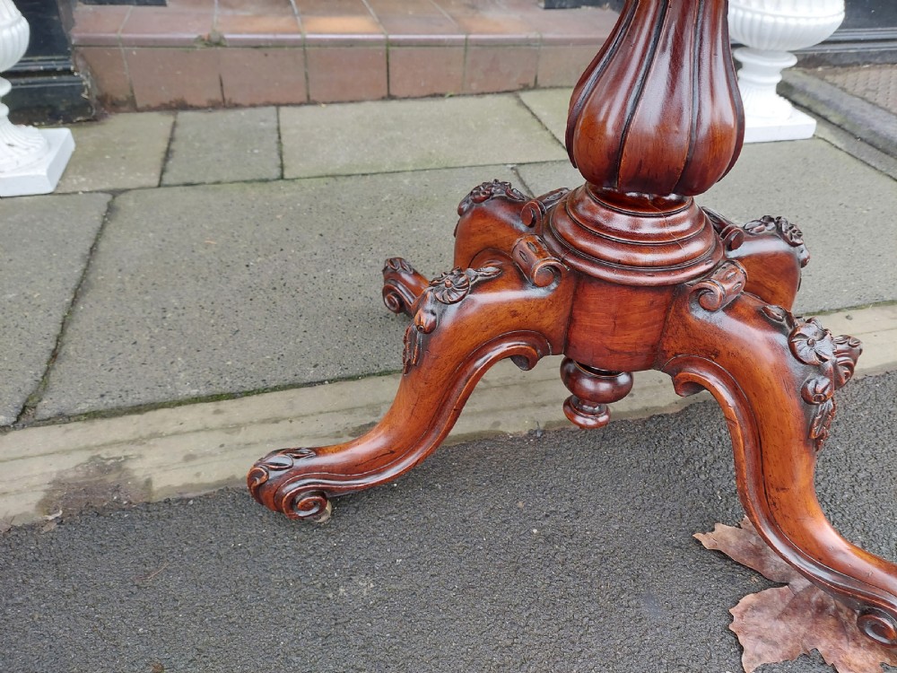 A Victorian burr walnut card table featuring a serpentine-shaped folding top resting on a carved pedestal support and quadripartite cabriole legs with castors. View IV