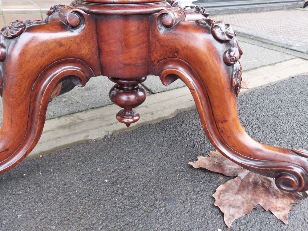 A Victorian burr walnut card table featuring a serpentine-shaped folding top resting on a carved pedestal support and quadripartite cabriole legs with castors. View V