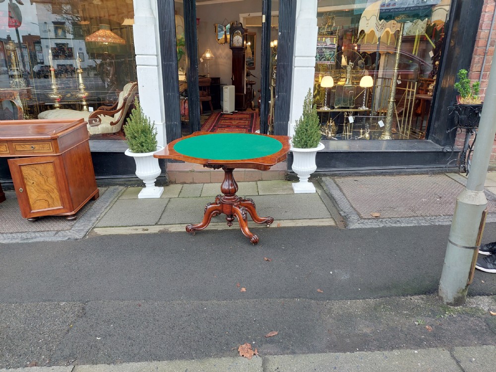 A Victorian burr walnut card table featuring a serpentine-shaped folding top resting on a carved pedestal support and quadripartite cabriole legs with castors. View VIII