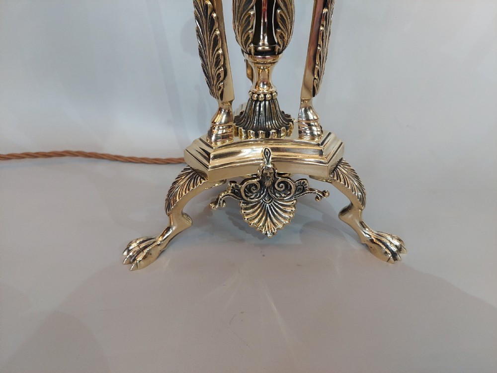 An early 20th-century brass table lamp featuring a central figure of Minerva flanked by stag head mounts, topped with a cream fringed lampshade. View II