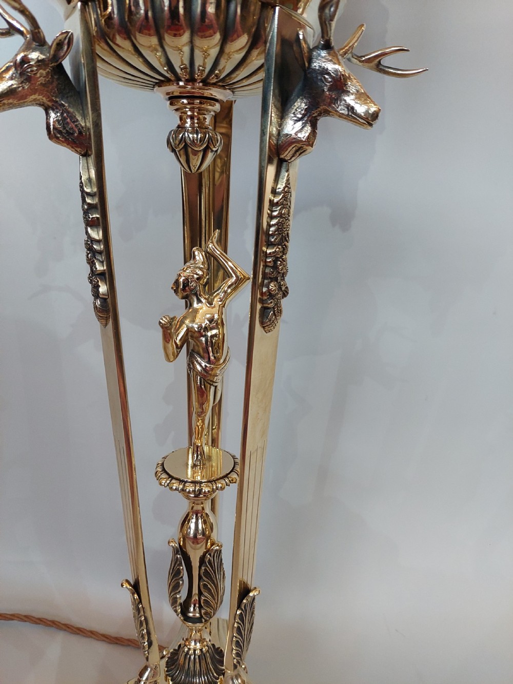 An early 20th-century brass table lamp featuring a central figure of Minerva flanked by stag head mounts, topped with a cream fringed lampshade. View IV