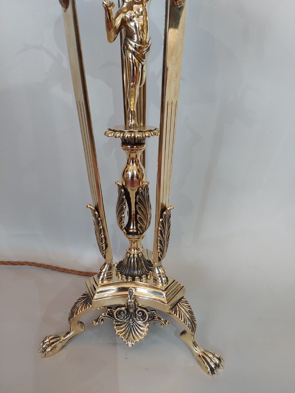An early 20th-century brass table lamp featuring a central figure of Minerva flanked by stag head mounts, topped with a cream fringed lampshade. View V
