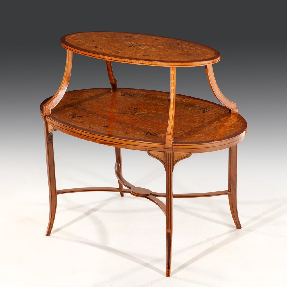 A two-tier oval mahogany side table featuring intricate floral marquetry inlay on both surfaces, slender curved supports, and an X-frame stretcher.