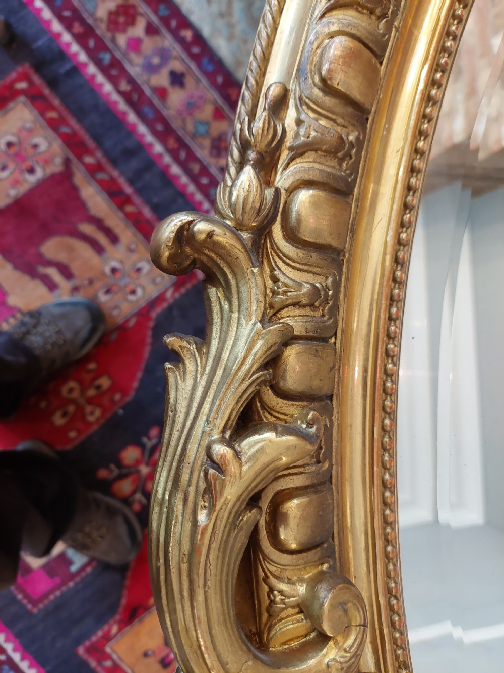 An oval Victorian Rococo style mirror featuring an ornate gilded frame with carved scrollwork, cresting, and egg-and-dart moulding. View III