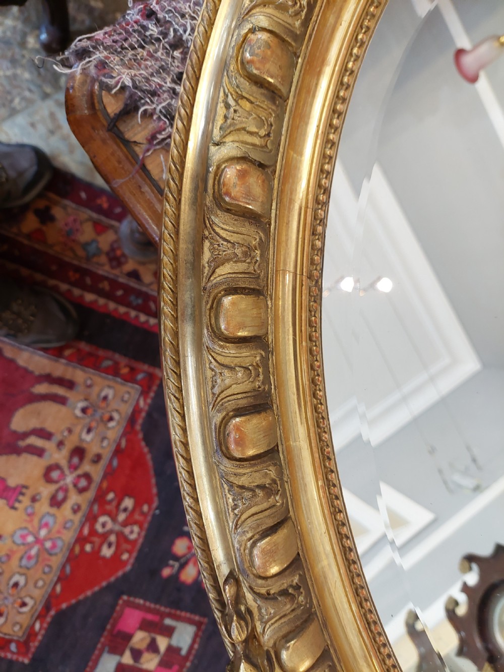 An oval Victorian Rococo style mirror featuring an ornate gilded frame with carved scrollwork, cresting, and egg-and-dart moulding. View IV