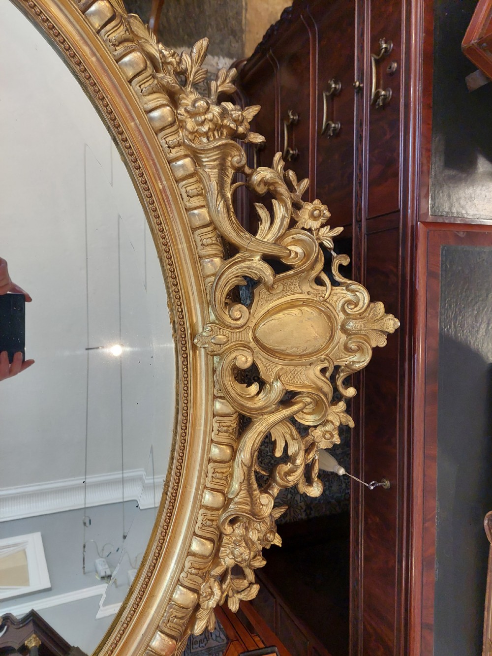 An oval Victorian Rococo style mirror featuring an ornate gilded frame with carved scrollwork, cresting, and egg-and-dart moulding. View VI