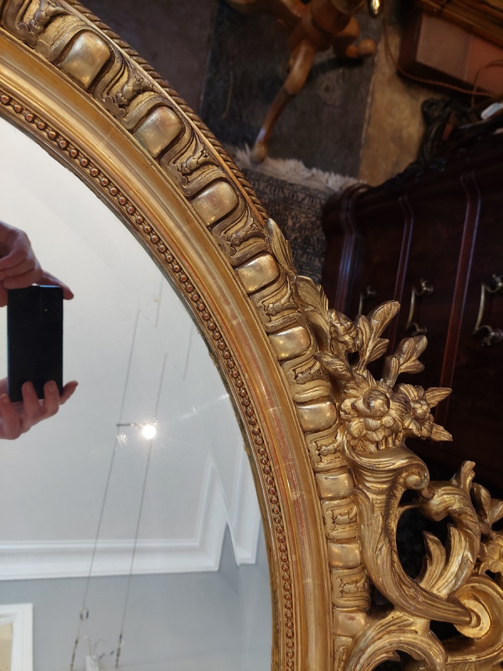 An oval Victorian Rococo style mirror featuring an ornate gilded frame with carved scrollwork, cresting, and egg-and-dart moulding. View VII