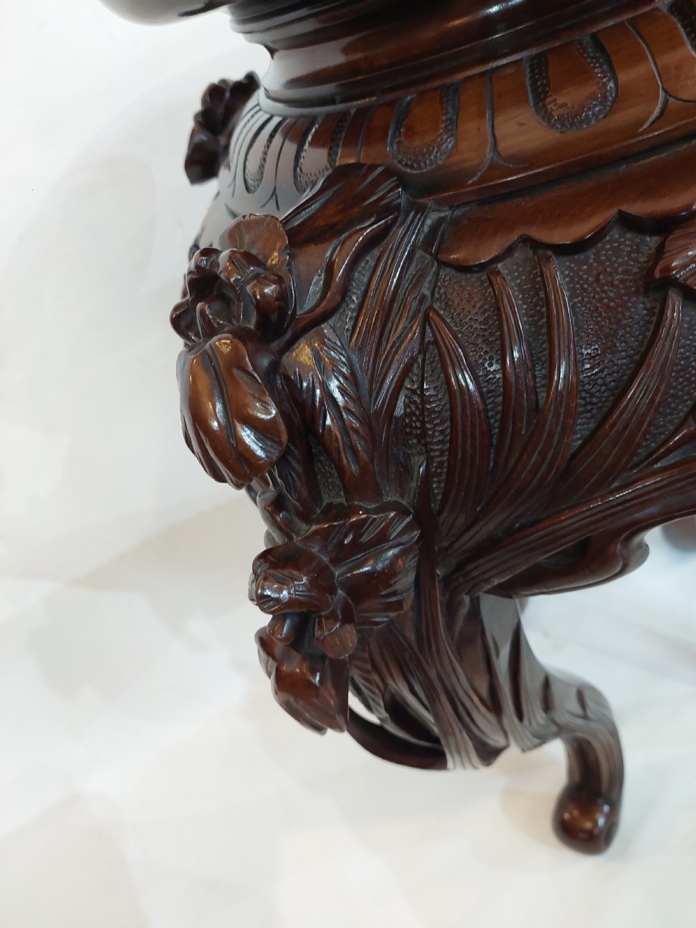 A dark mahogany circular jardiniere stand featuring elaborate floral relief carving around the deep apron and sweeping cabriole legs. View II
