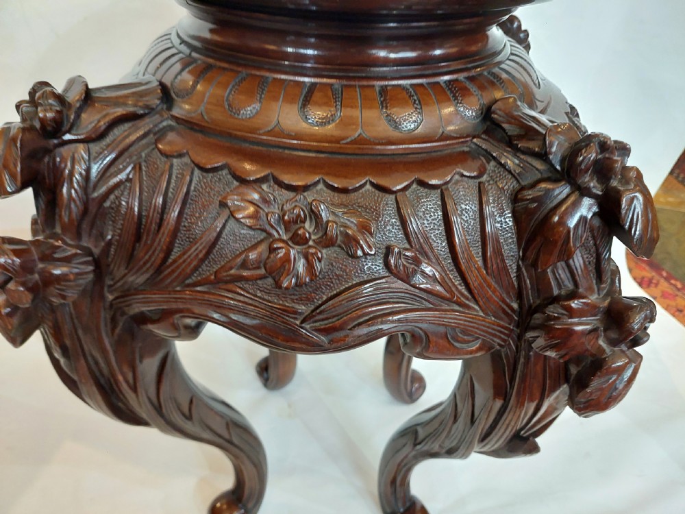 A dark mahogany circular jardiniere stand featuring elaborate floral relief carving around the deep apron and sweeping cabriole legs. View III