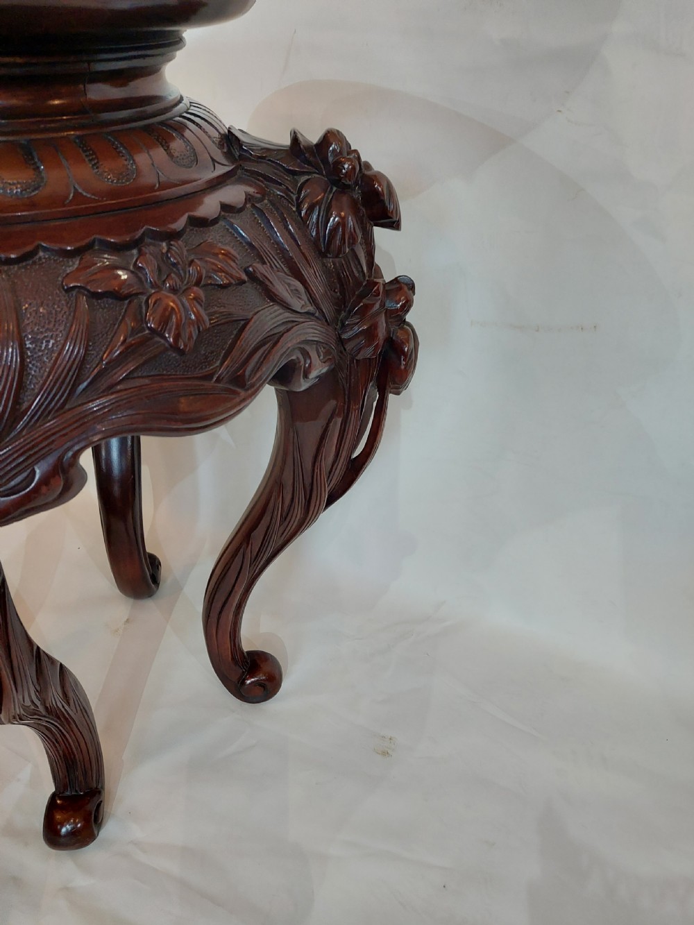 A dark mahogany circular jardiniere stand featuring elaborate floral relief carving around the deep apron and sweeping cabriole legs. View X