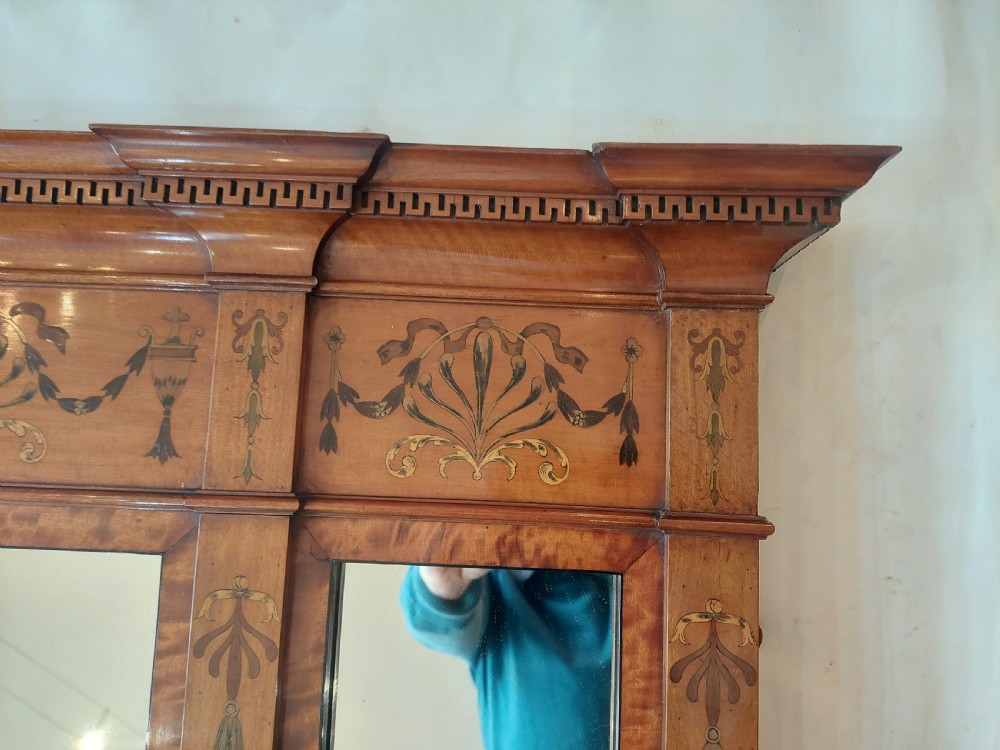 A wide satinwood overmantel mirror featuring three glass panels surrounded by a frame decorated with painted foliage swags and husk garlands. View II