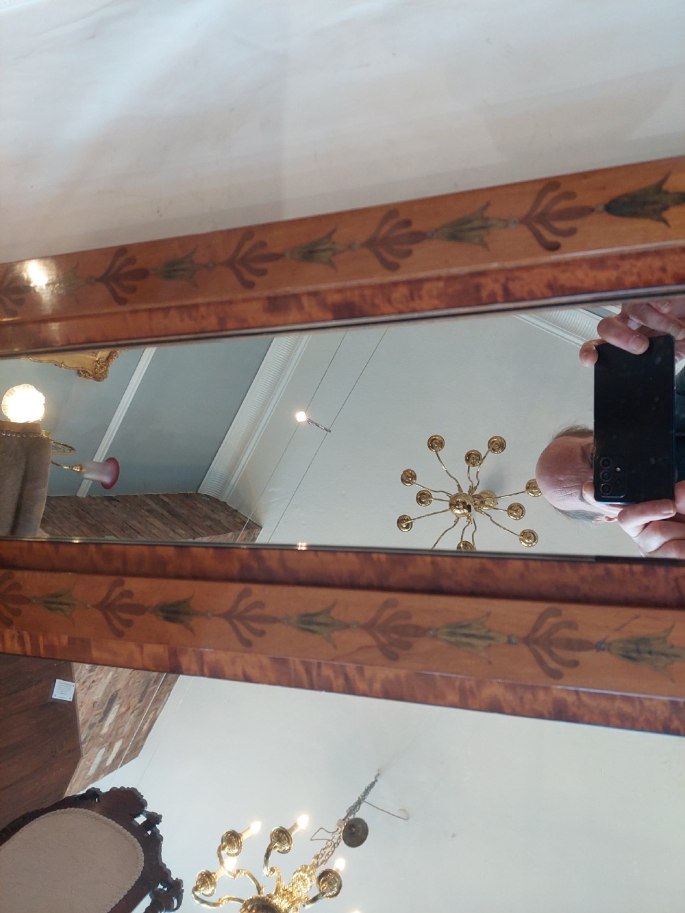A wide satinwood overmantel mirror featuring three glass panels surrounded by a frame decorated with painted foliage swags and husk garlands. View V