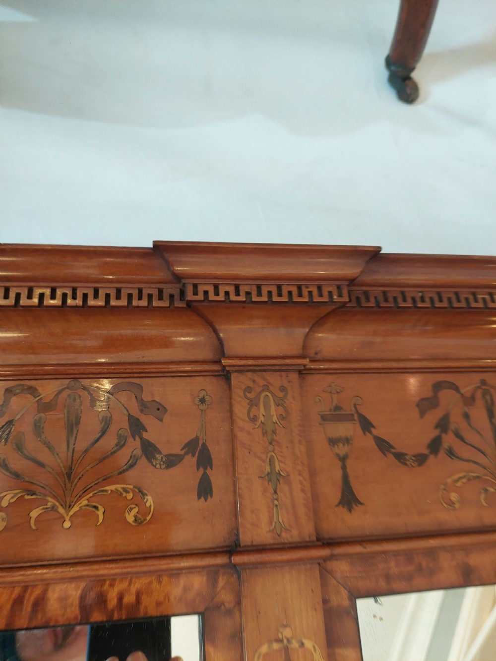 A wide satinwood overmantel mirror featuring three glass panels surrounded by a frame decorated with painted foliage swags and husk garlands. View VI