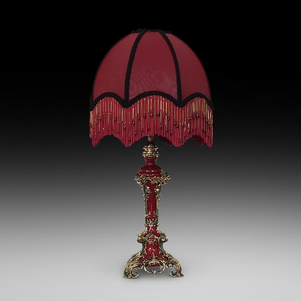 A late nineteenth-century Rococo Revival table lamp featuring a red glazed body with ornate gilt bronze scroll mounts and a red beaded fringe dome shade.