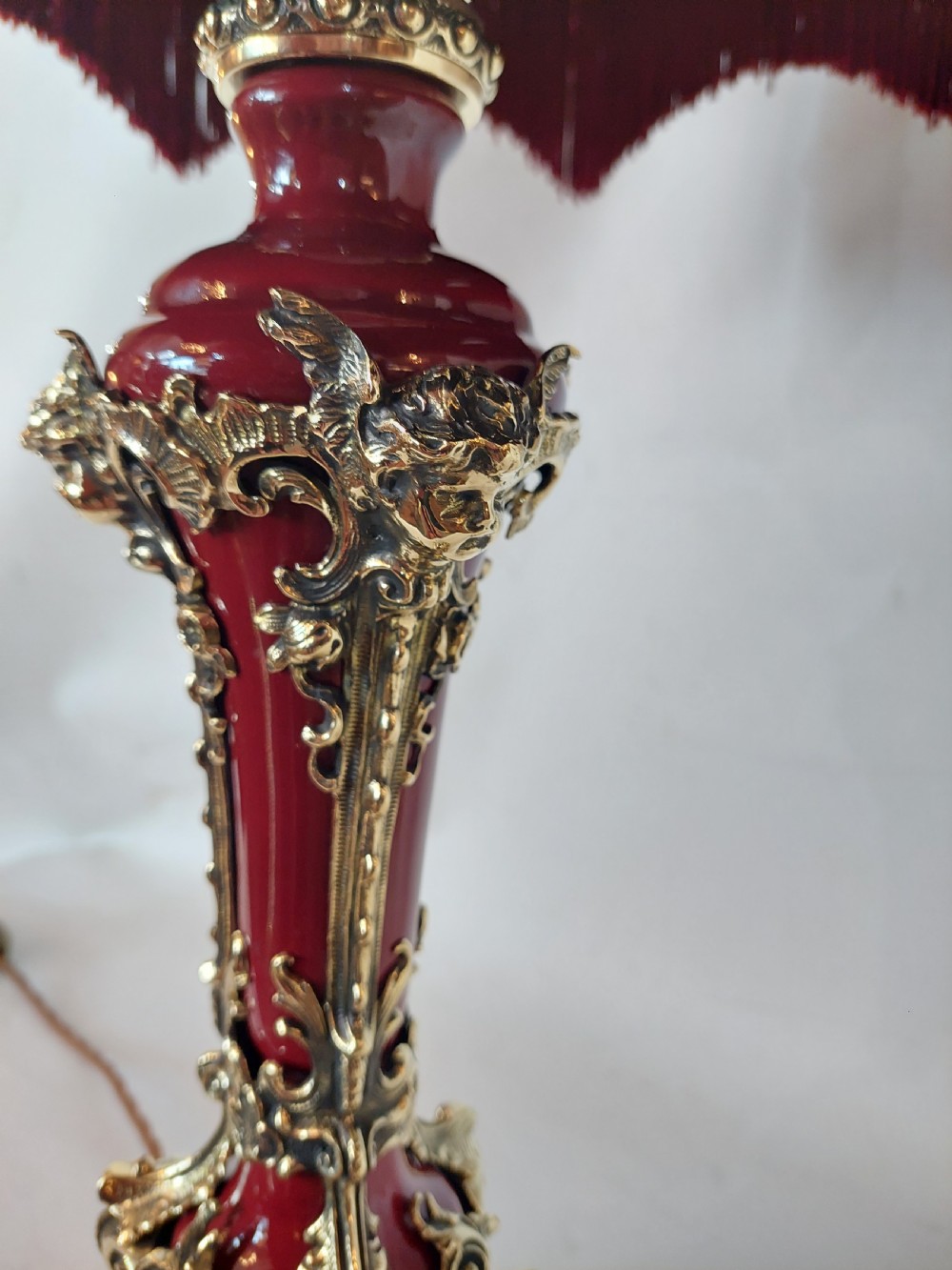 A late nineteenth-century Rococo Revival table lamp featuring a red glazed body with ornate gilt bronze scroll mounts and a red beaded fringe dome shade. View IV