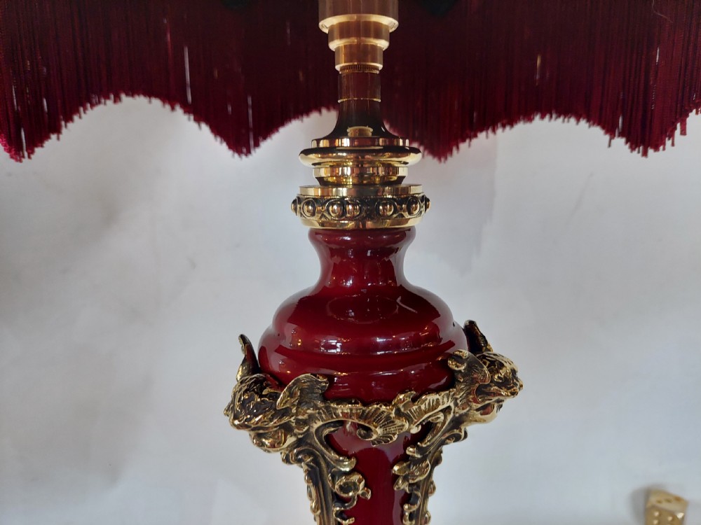 A late nineteenth-century Rococo Revival table lamp featuring a red glazed body with ornate gilt bronze scroll mounts and a red beaded fringe dome shade. View V