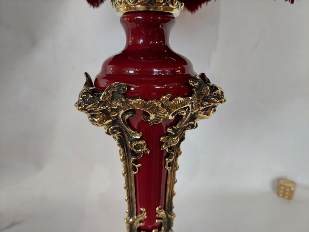 A late nineteenth-century Rococo Revival table lamp featuring a red glazed body with ornate gilt bronze scroll mounts and a red beaded fringe dome shade. View VI