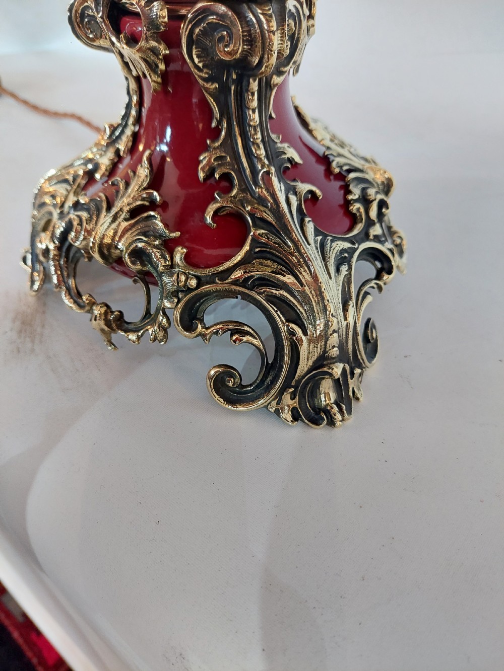 A late nineteenth-century Rococo Revival table lamp featuring a red glazed body with ornate gilt bronze scroll mounts and a red beaded fringe dome shade. View VII
