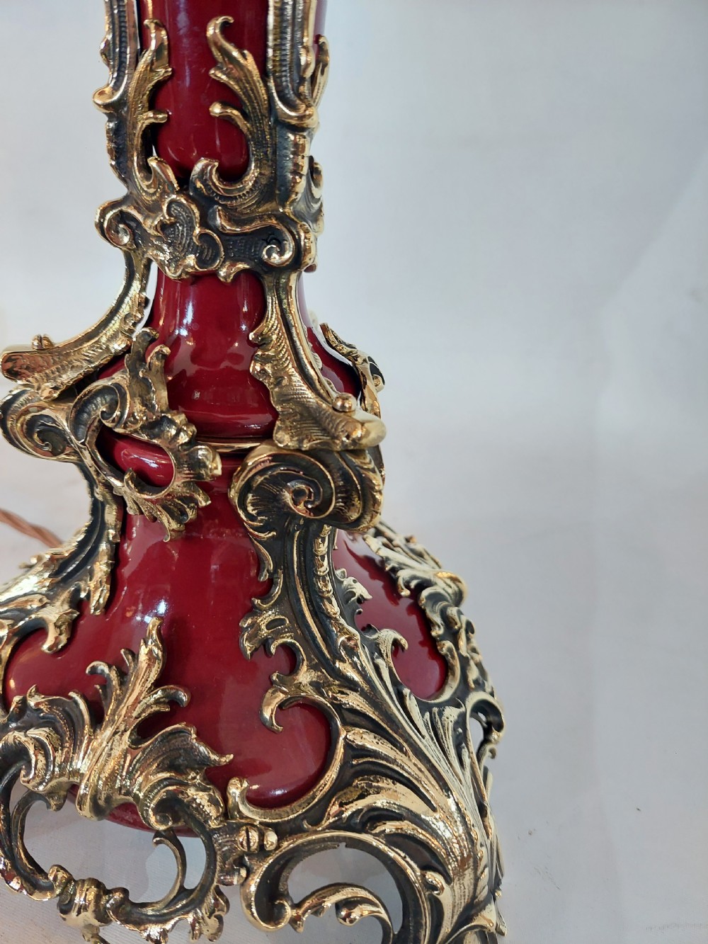 A late nineteenth-century Rococo Revival table lamp featuring a red glazed body with ornate gilt bronze scroll mounts and a red beaded fringe dome shade. View X