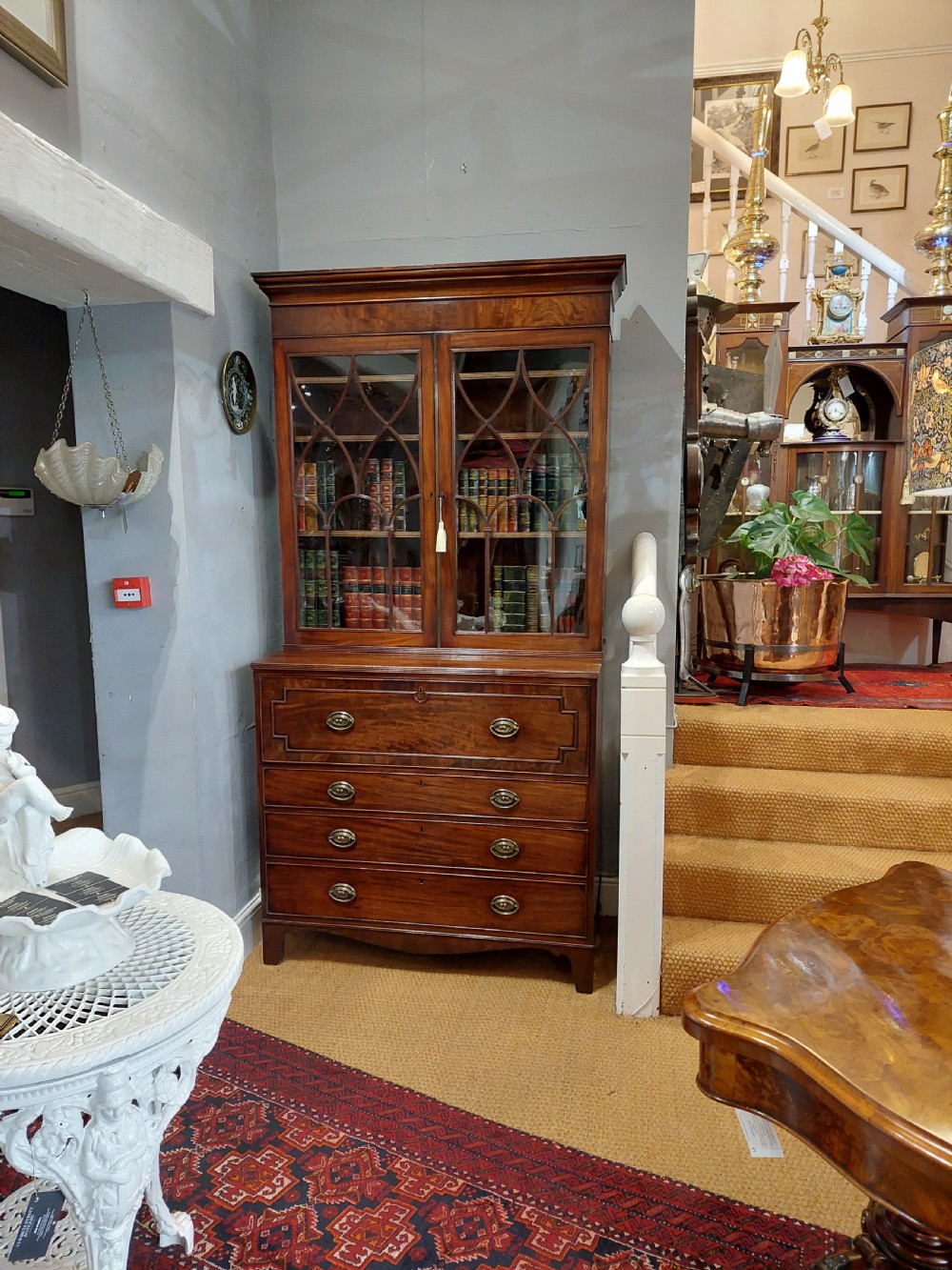 A tall Regency mahogany secretaire bookcase featuring two upper glazed doors with intricate geometric glazing bars above a chest of drawers with oval brass handles. View III