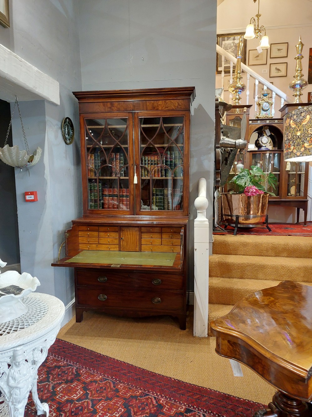 A tall Regency mahogany secretaire bookcase featuring two upper glazed doors with intricate geometric glazing bars above a chest of drawers with oval brass handles. View V
