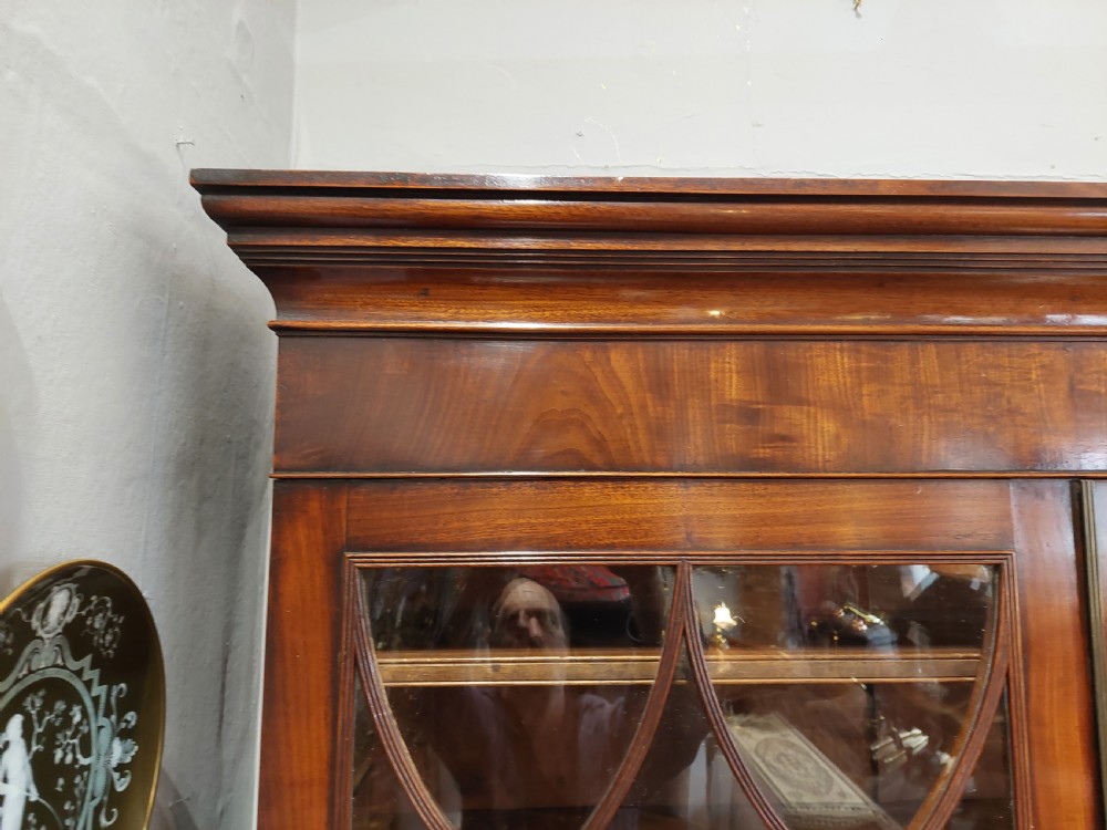 A tall Regency mahogany secretaire bookcase featuring two upper glazed doors with intricate geometric glazing bars above a chest of drawers with oval brass handles. View XI