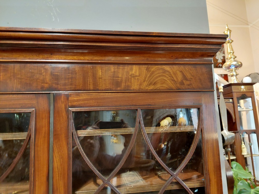 A tall Regency mahogany secretaire bookcase featuring two upper glazed doors with intricate geometric glazing bars above a chest of drawers with oval brass handles. View XII