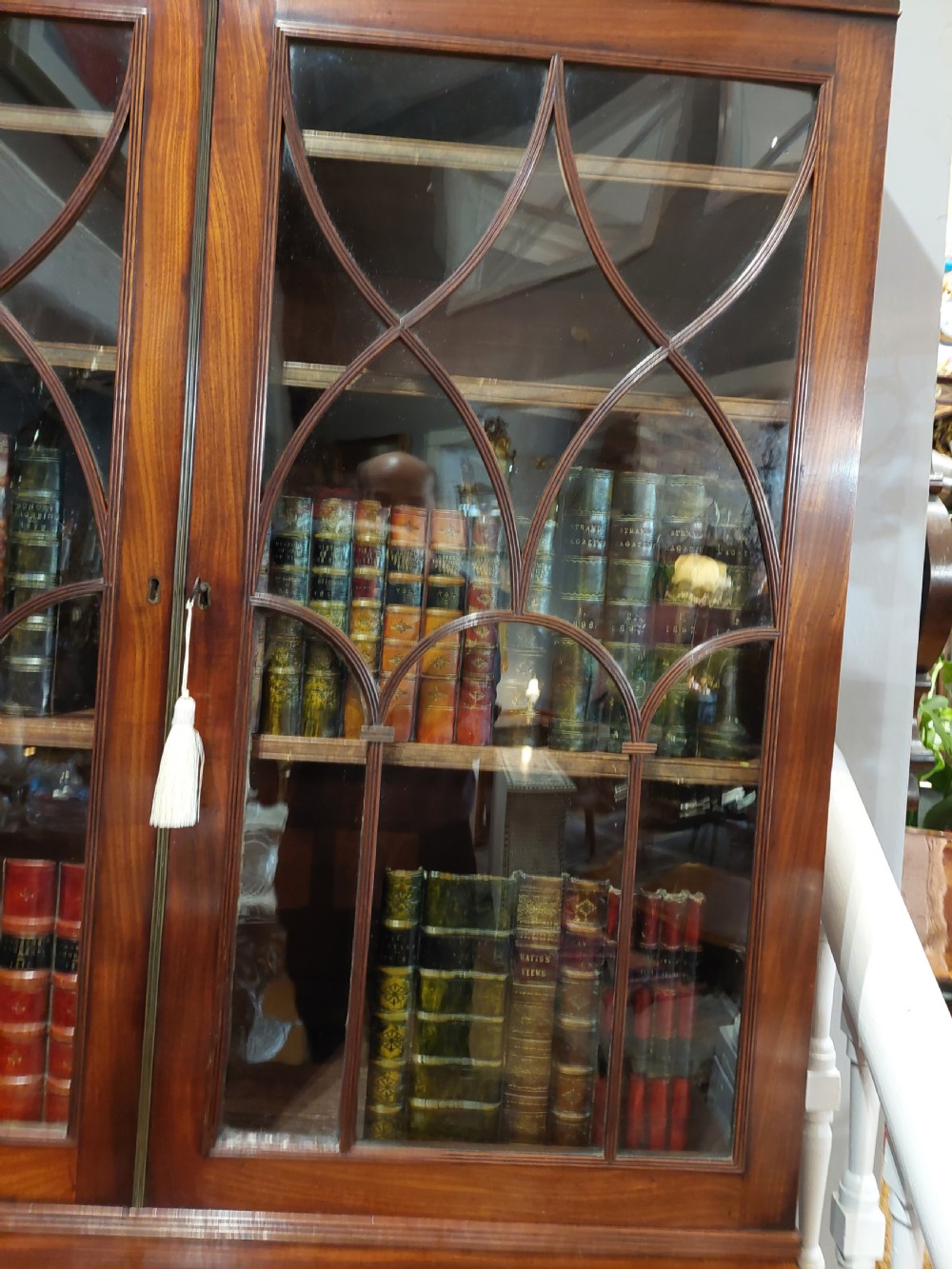 A tall Regency mahogany secretaire bookcase featuring two upper glazed doors with intricate geometric glazing bars above a chest of drawers with oval brass handles. View XIV