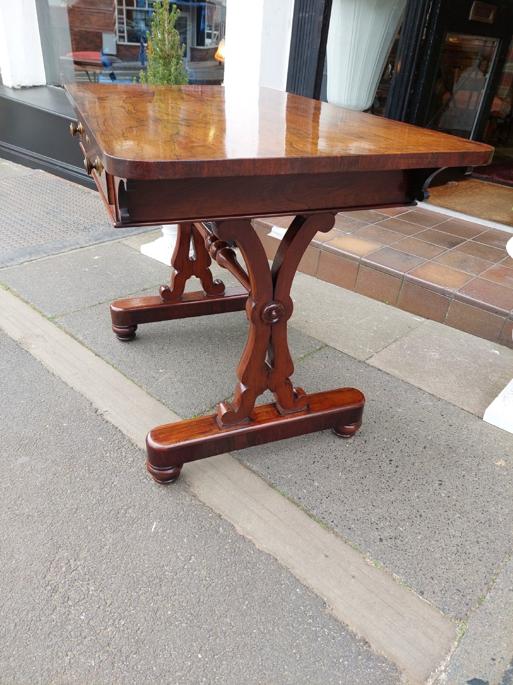 A Regency rosewood sofa table featuring a figured timber top, single frieze drawer with brass knobs, a turned central stretcher, and trestle legs. View III