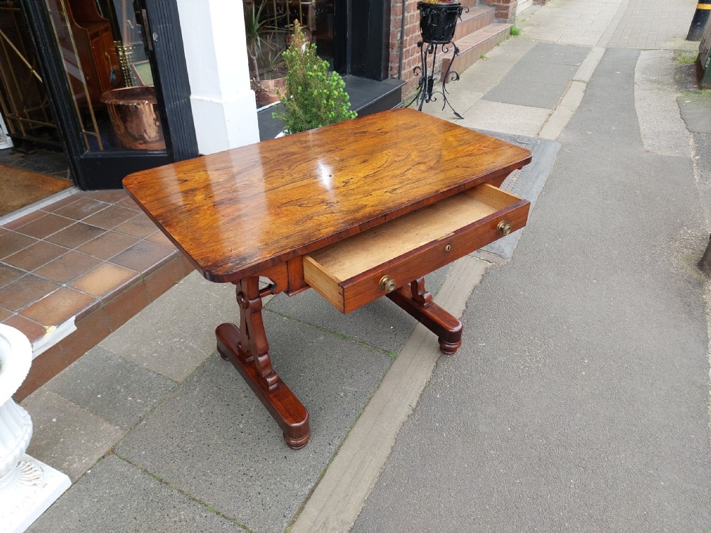 A Regency rosewood sofa table featuring a figured timber top, single frieze drawer with brass knobs, a turned central stretcher, and trestle legs. View VI