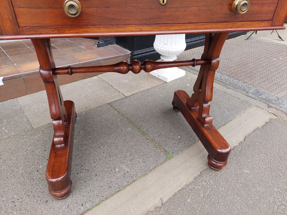 A Regency rosewood sofa table featuring a figured timber top, single frieze drawer with brass knobs, a turned central stretcher, and trestle legs. View IX