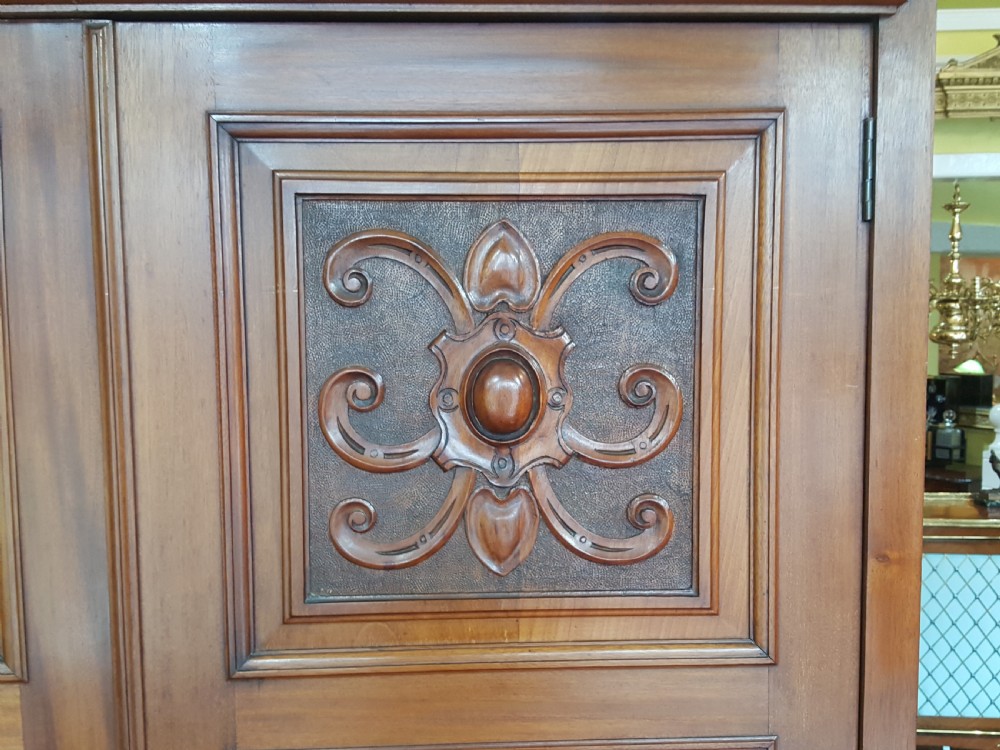 An Arts and Crafts mahogany hall robe featuring carved upper panels, two full-length doors, and a shaped top crest with corner finials. View II