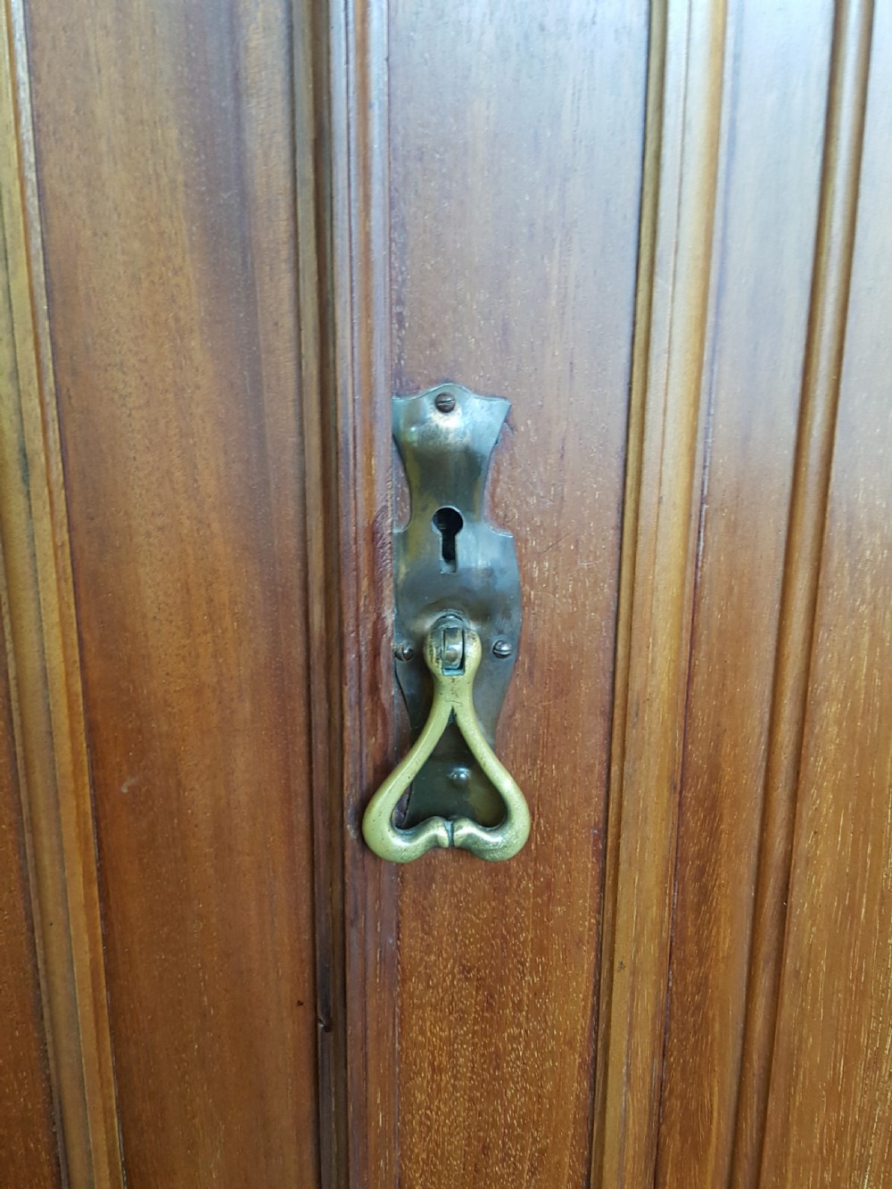 An Arts and Crafts mahogany hall robe featuring carved upper panels, two full-length doors, and a shaped top crest with corner finials. View V